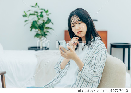 A young woman is troubled while using her smartphone in the living room. A young woman is troubled while using her smartphone in the living room. 140727440