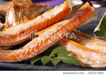 A dish featuring beautifully grilled salmon belly with plenty of fat, layered on a black plate. A dish featuring beautifully grilled salmon belly with plenty of fat, layered on a black plate. 140727469