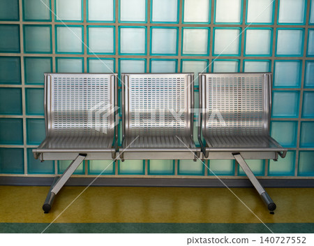 Three metal seats in an empty waiting area against a glass block wall Three metal seats in an empty waiting area against a glass block wall 140727552