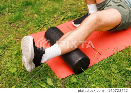 Close-up of a fit man performing myofascial release on a calf with a foam roller. Outdoor self-massage for muscle recovery, tension relief, and post-workout recovery. Close-up of a fit man performing myofascial release on a calf with a foam roller. Outdoor self-massage for muscle recovery, tension relief, and post-workout recovery. 140728452