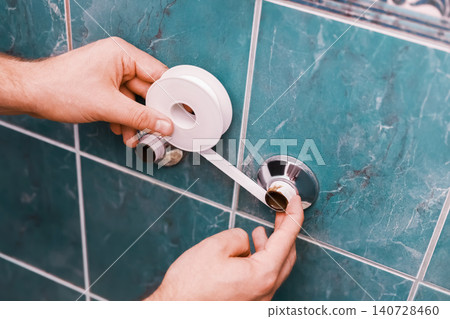 Homeowner replacing an old faucet during a DIY plumbing repair. Hands applying thread sealant tape on pipes for a bathroom home renovation. 140728460