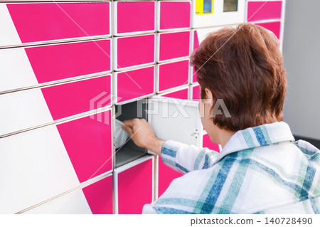 Man using a self-service parcel locker terminal for package pickup. Concept of online shopping, ecommerce, and contactless delivery logistics service. Man using a self-service parcel locker terminal for package pickup. Concept of online shopping, ecommerce, and contactless delivery logistics service. 140728490