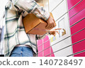 Man holding packages using a touchscreen at a bright pink parcel locker terminal. Convenient self-service technology for ecommerce delivery and contactless pickup. 140728497