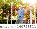 Man doing pullups on outdoor calisthenics bars during a fitness workout in a sunny park. Athlete training bodyweight exercise. 140728511