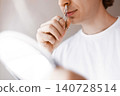 Close up of a man using a manual metal trimmer for nose hair removal. Male facial care, hygiene, and daily grooming routine concept with a mirror. 140728514
