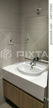A modern bathroom interior featuring a white ceramic sink mounted above a minimalist vanity cabinet with a wall mirror and chrome faucet. A modern bathroom interior featuring a white ceramic sink mounted above a minimalist vanity cabinet with a wall mirror and chrome faucet. 140728565