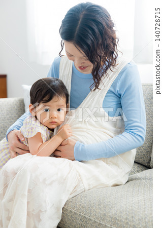 一位懷孕的母親抱著她一歲的女兒。 一位懷孕的母親抱著她一歲的女兒。 140728715