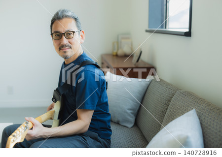 一位老人在沙發上彈吉他。 一位老人在沙發上彈吉他。 140728916