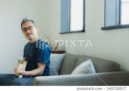 一位老人在沙發上彈吉他。 一位老人在沙發上彈吉他。 140728917