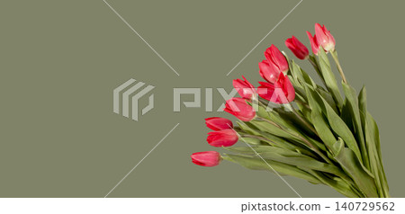 Large bouquet of many red tulip flowers arranged with green leaves on green background with copy space. Multiple blooms grouped forming dense arrangement with empty area for text. Floral 140729562