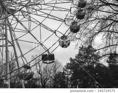 Ferris wheel structure rises in monochrome with visible cabins detail. Amusement ride forms geometric pattern against sky dramatic composition Ferris wheel structure rises in monochrome with visible cabins detail. Amusement ride forms geometric pattern against sky dramatic composition 140729575