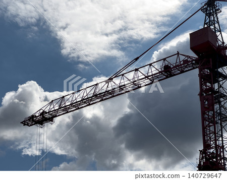 Tower crane against dramatic clouds. Industrial construction equipment rises into a blue sky. Infrastructure and engineering background.. Tower crane against dramatic clouds. Industrial construction equipment rises into a blue sky. Infrastructure and engineering background.. 140729647