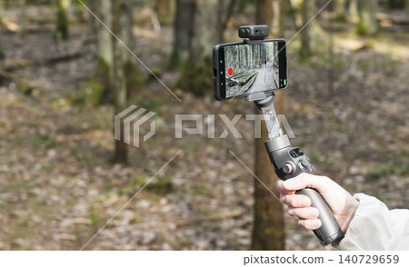 Smartphone on a handheld gimbal in a forest. Mobile video recording setup for outdoor content creation. Travel and hiking technology in nature.. Smartphone on a handheld gimbal in a forest. Mobile video recording setup for outdoor content creation. Travel and hiking technology in nature.. 140729659