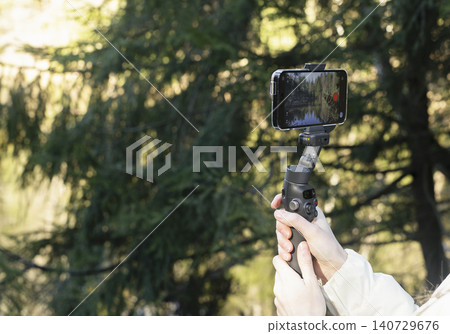 Smartphone on a gimbal in a forest. Handheld mobile video setup for outdoor filming. Content creation gear for travel and vlogging.. Smartphone on a gimbal in a forest. Handheld mobile video setup for outdoor filming. Content creation gear for travel and vlogging.. 140729676