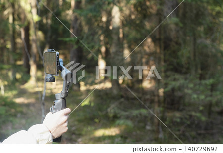 Smartphone mounted on a gimbal in a forest. Mobile video recording gear in a woodland setting. Outdoor content creation setup for vlogging and travel footage.. Smartphone mounted on a gimbal in a forest. Mobile video recording gear in a woodland setting. Outdoor content creation setup for vlogging and travel footage.. 140729692