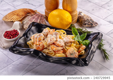 Shrimp pasta with cream sauce, lemon, and herbs in black bowl on marble table Shrimp pasta with cream sauce, lemon, and herbs in black bowl on marble table 140729945