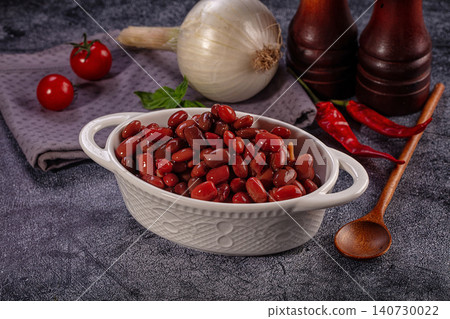 Red kidney beans in white ceramic bowl with onion tomatoes chili peppers wooden spoon and spice mills on dark grey stone surface culinary composition healthy vegetarian protein source Red kidney beans in white ceramic bowl with onion tomatoes chili peppers wooden spoon and spice mills on dark grey stone surface culinary composition healthy vegetarian protein source 140730022