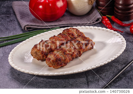 Grilled meat skewers on white plate with tomato onion and chili peppers Grilled meat skewers on white plate with tomato onion and chili peppers 140730026