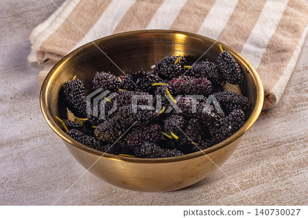 Fresh dark mulberries in brass bowl on striped linen Fresh dark mulberries in brass bowl on striped linen 140730027