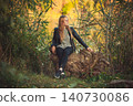 Pensive woman in leather jacket sitting on log in autumn nature 140730086