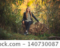 Young blonde woman in leather jacket sitting on tree stump in autumn forest 140730087