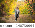 Blonde woman walking park path during golden autumn evening. Relaxed adult outdoors enjoying warm fall light 140730094