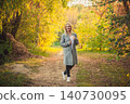 Smiling blonde woman walking autumn forest path, vibrant fall foliage, happy mood, natural light 140730095