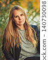 Portrait of calm young woman with long blonde hair and green eyes outdoors in autumn 140730098
