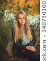 Portrait of young blonde woman in black leather jacket sitting outdoors in autumn park 140730100