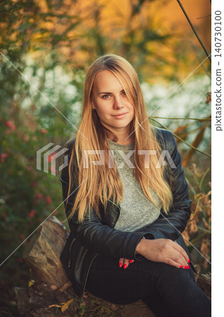 Portrait of young blonde woman in black leather jacket sitting outdoors in autumn park Portrait of young blonde woman in black leather jacket sitting outdoors in autumn park 140730100