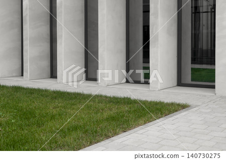 Concrete columns and green lawn near modern building facade in minimalist style. Linear structure creates rhythm with repeating vertical elements. Concept of contemporary architecture 140730275