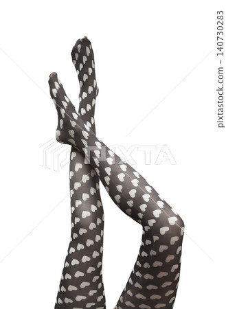 Female legs crossed wearing heart pattern tights isolated white background. Fashion hosiery shown in dynamic pose with decorative print. Concept of stylish clothing aesthetic.. 140730283