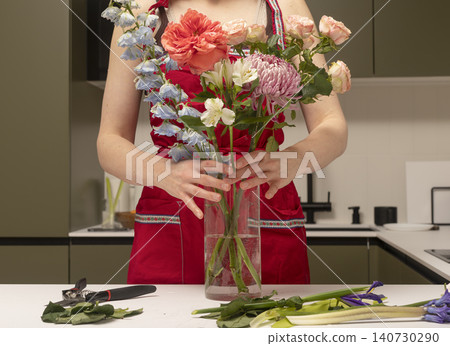 Florist arranging bouquet of different flowers in vase at table. Hands composing floral arrangement with stems and blossoms. Concept of flower design and decoration.. Florist arranging bouquet of different flowers in vase at table. Hands composing floral arrangement with stems and blossoms. Concept of flower design and decoration.. 140730290