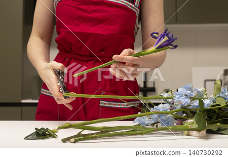 Florist cutting flower stem with pruning shears during preparation. Hands working with plants arranging bouquet elements on table. Concept of floral craft and design.. Florist cutting flower stem with pruning shears during preparation. Hands working with plants arranging bouquet elements on table. Concept of floral craft and design.. 140730292