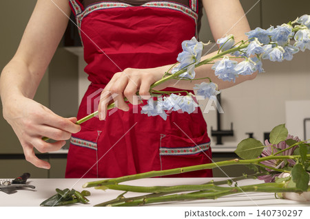 Florist holding flower stem and removing leaves before arrangement. Hands preparing plant material for bouquet composition. Concept of floral design process.. Florist holding flower stem and removing leaves before arrangement. Hands preparing plant material for bouquet composition. Concept of floral design process.. 140730297