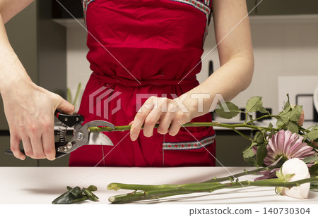 Florist trimming long stem using pruning shears at workspace. Hands processing plant material for floral arrangement. Concept of flower preparation and care.. Florist trimming long stem using pruning shears at workspace. Hands processing plant material for floral arrangement. Concept of flower preparation and care.. 140730304