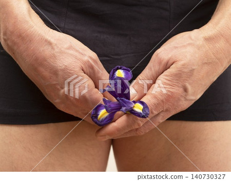 Male hands holding iris flower near body symbolizing reproductive health. Concept of male wellness fertility and urogenital system awareness. Intimate health care representation.. Male hands holding iris flower near body symbolizing reproductive health. Concept of male wellness fertility and urogenital system awareness. Intimate health care representation.. 140730327
