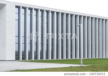 Modern low building with repeating concrete columns and glass facade near green lawn. Minimalist architecture structure with geometric rhythm and linear perspective. Concept of urban design Modern low building with repeating concrete columns and glass facade near green lawn. Minimalist architecture structure with geometric rhythm and linear perspective. Concept of urban design 140730351