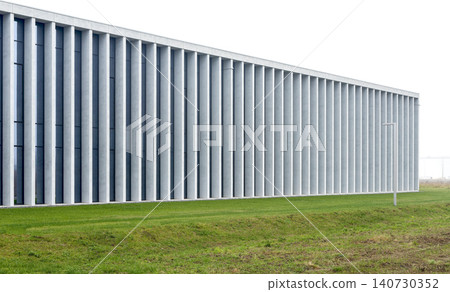 Modern minimalist building with long facade and concrete columns near green lawn. Linear structure extending horizontally with repeating elements. Concept of contemporary architecture urban Modern minimalist building with long facade and concrete columns near green lawn. Linear structure extending horizontally with repeating elements. Concept of contemporary architecture urban 140730352