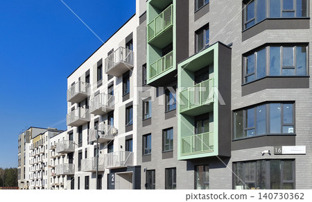 Modern residential building with layered balconies and geometric facade composition. Apartment structure shows clean design and urban architecture style. Concept of housing development Modern residential building with layered balconies and geometric facade composition. Apartment structure shows clean design and urban architecture style. Concept of housing development 140730362
