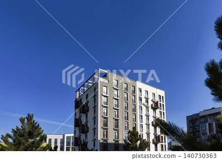 Modern residential building with rooftop terrace under clear blue sky. Contemporary structure shows clean facade and minimal composition. Concept of urban housing architecture development.. Modern residential building with rooftop terrace under clear blue sky. Contemporary structure shows clean facade and minimal composition. Concept of urban housing architecture development.. 140730363