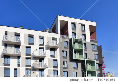 Modern residential building with white facade and green balcony accents. Apartment structure shows geometric composition and minimal design. Concept of contemporary housing architecture.. Modern residential building with white facade and green balcony accents. Apartment structure shows geometric composition and minimal design. Concept of contemporary housing architecture.. 140730364