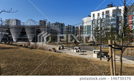 Modern residential complex with public space and seating areas in urban environment. Buildings form geometric composition with open landscape. Concept of contemporary housing community Modern residential complex with public space and seating areas in urban environment. Buildings form geometric composition with open landscape. Concept of contemporary housing community 140730370