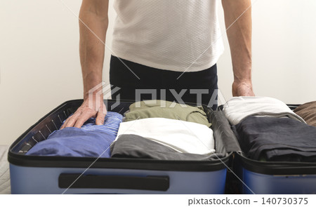 Person arranging clothes inside suitcase during packing process for travel. Hands place garments in organized layout within luggage. Concept of trip preparation organization.. Person arranging clothes inside suitcase during packing process for travel. Hands place garments in organized layout within luggage. Concept of trip preparation organization.. 140730375