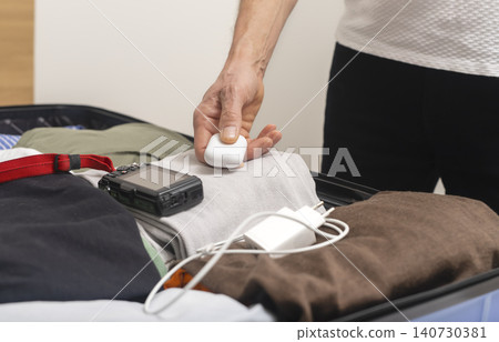 Person packing electronics including camera charger and earphones case into suitcase. Hands arrange gadgets and accessories inside luggage. Concept of travel preparation technology equipment Person packing electronics including camera charger and earphones case into suitcase. Hands arrange gadgets and accessories inside luggage. Concept of travel preparation technology equipment 140730381