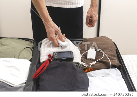 Person placing electronic accessories and earphones case into suitcase during packing. Hands organize gadgets neatly inside luggage. Concept of travel preparation equipment arrangement.. Person placing electronic accessories and earphones case into suitcase during packing. Hands organize gadgets neatly inside luggage. Concept of travel preparation equipment arrangement.. 140730385