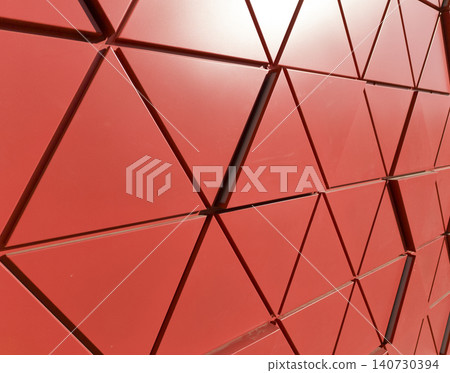 Red geometric facade with triangular panels forming dynamic architectural pattern. Surface structure creates depth and bold composition. Concept of modern design abstract exterior detail.. Red geometric facade with triangular panels forming dynamic architectural pattern. Surface structure creates depth and bold composition. Concept of modern design abstract exterior detail.. 140730394