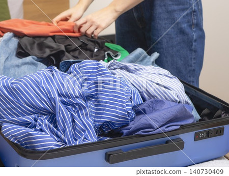 Woman arranging disorganized clothes inside open suitcase before travel. Hands place garments in chaotic way during packing process. Concept of messy preparation for trip.. Woman arranging disorganized clothes inside open suitcase before travel. Hands place garments in chaotic way during packing process. Concept of messy preparation for trip.. 140730409