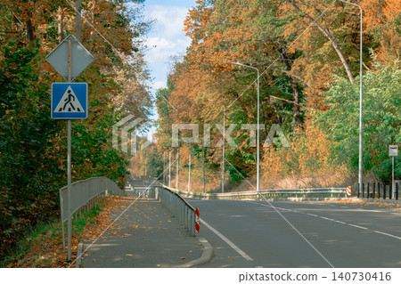 Autumn road lined with vibrant trees and pedestrian crossing sign Autumn road lined with vibrant trees and pedestrian crossing sign 140730416