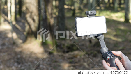 Smartphone mounted on a gimbal in a forest. Handheld stabilizer for mobile filming and vlogging. Outdoor content creation gear with copy space.. 140730472